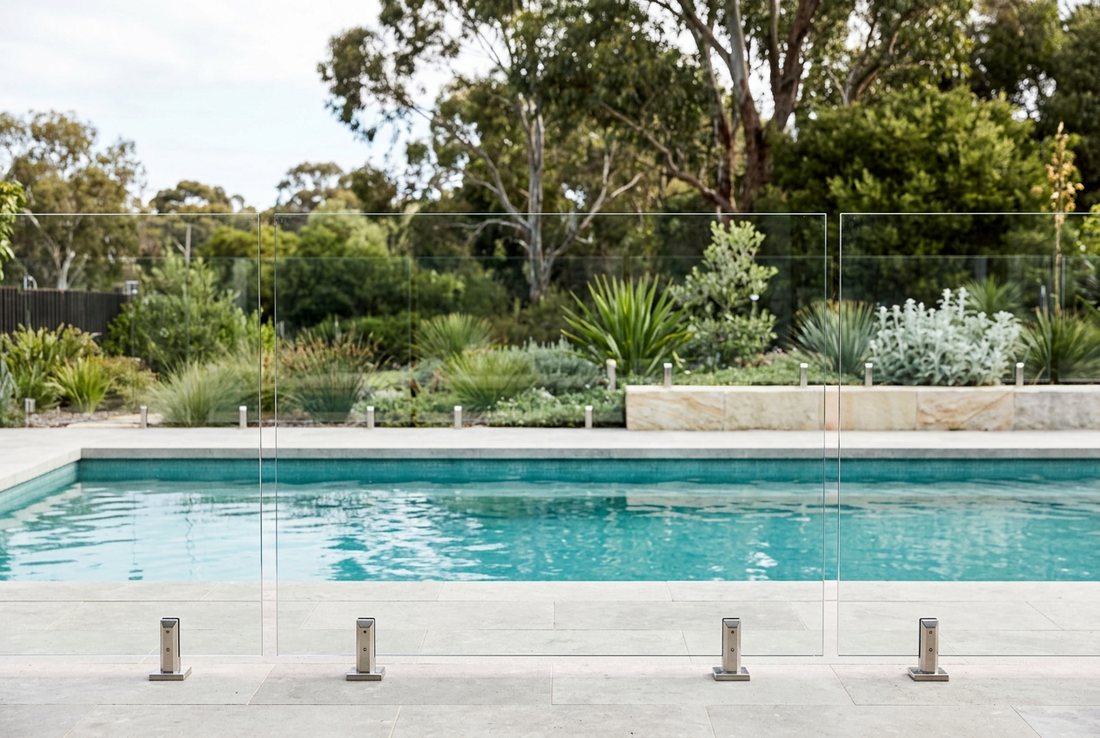 Frameless glass pool fence with rectangular panels beside a swimming pool.